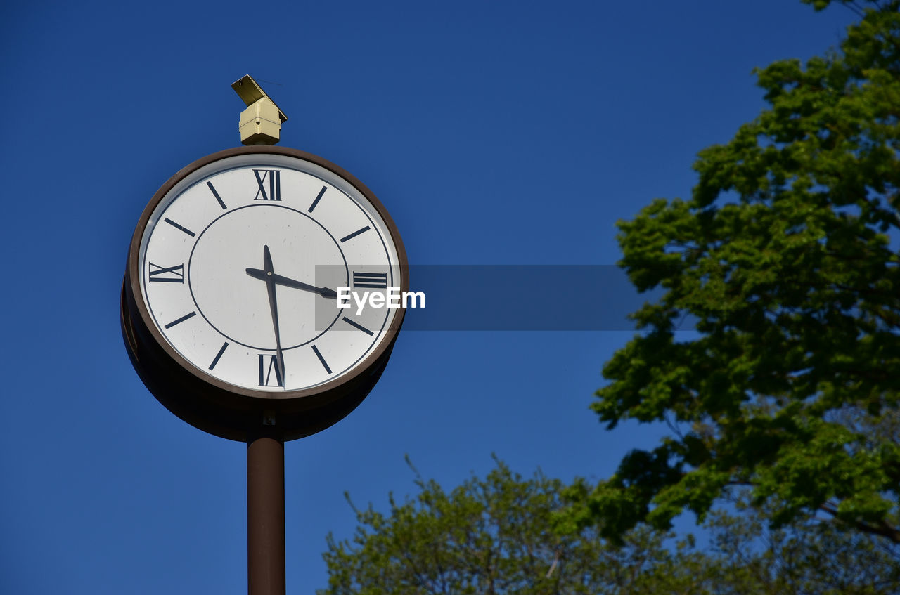 Low angle view of clock against clear blue sky