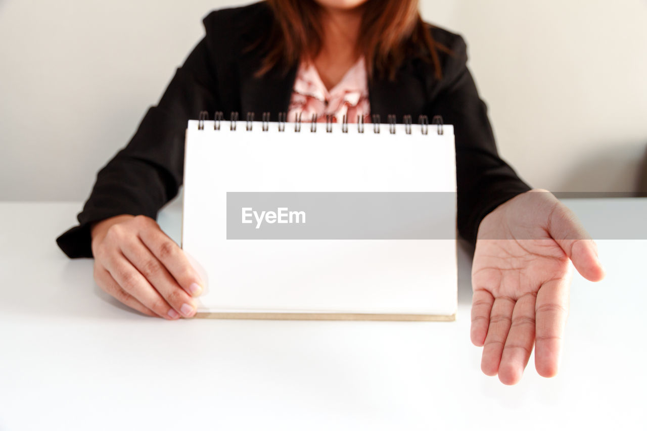 Midsection of businesswoman showing blank spiral notebook at table