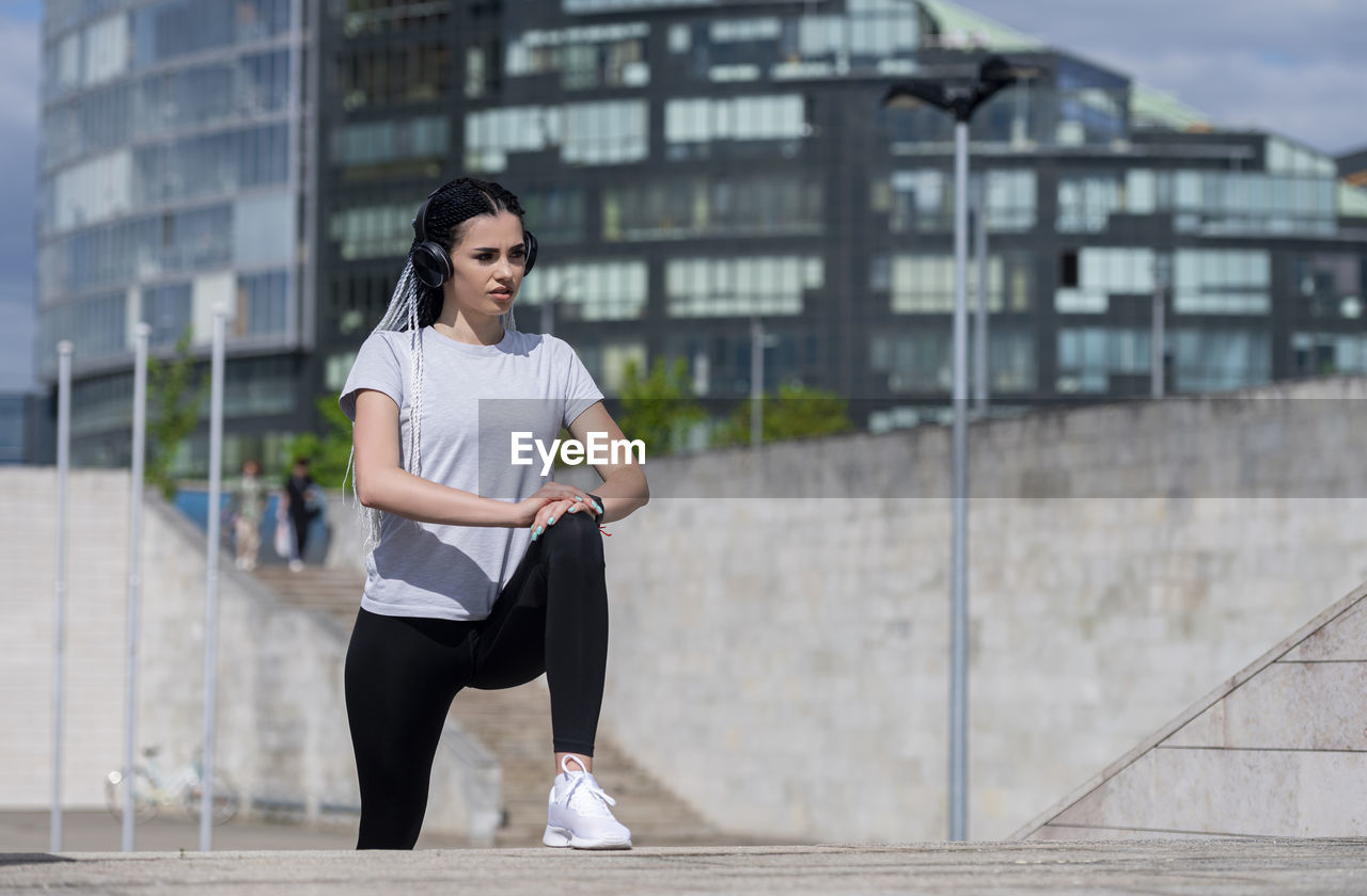 FULL LENGTH PORTRAIT OF YOUNG WOMAN IN CITY BUILDINGS