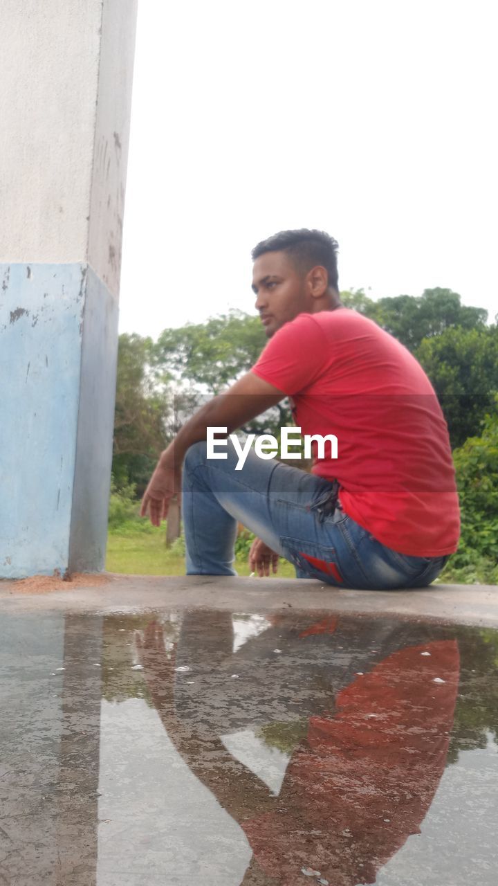 SIDE VIEW OF A YOUNG MAN SITTING ON WALL
