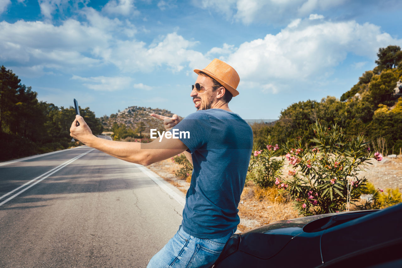 Man taking selfie while standing on road against sky