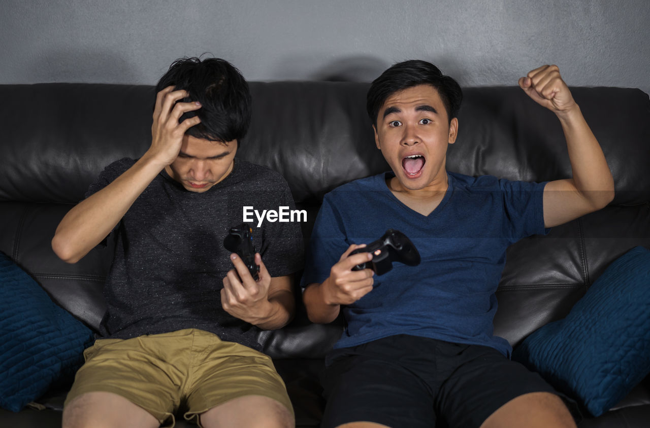 YOUNG MAN USING MOBILE PHONE WHILE SITTING ON SOFA