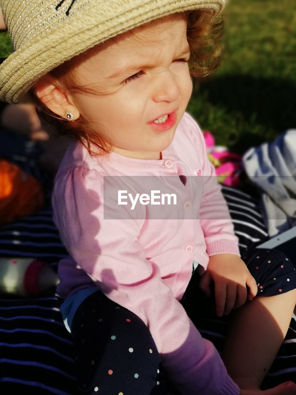 High angle view of cute baby girl wearing hat sitting in park during sunny day