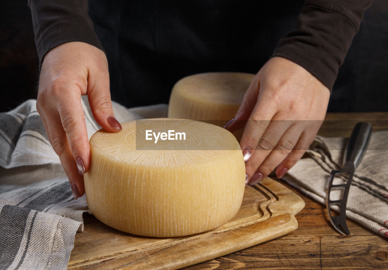 Somebody hands put a wheel of fresh homemade cheese on a wooden board close up