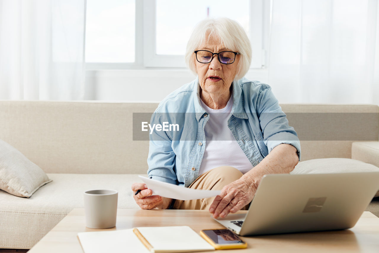 Senior woman holding paper sitting with laptop at home