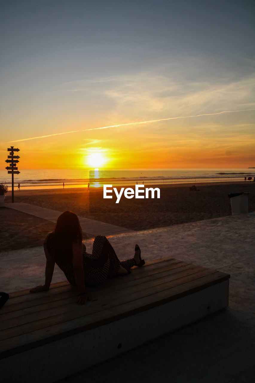 PEOPLE SITTING ON BEACH AT SUNSET