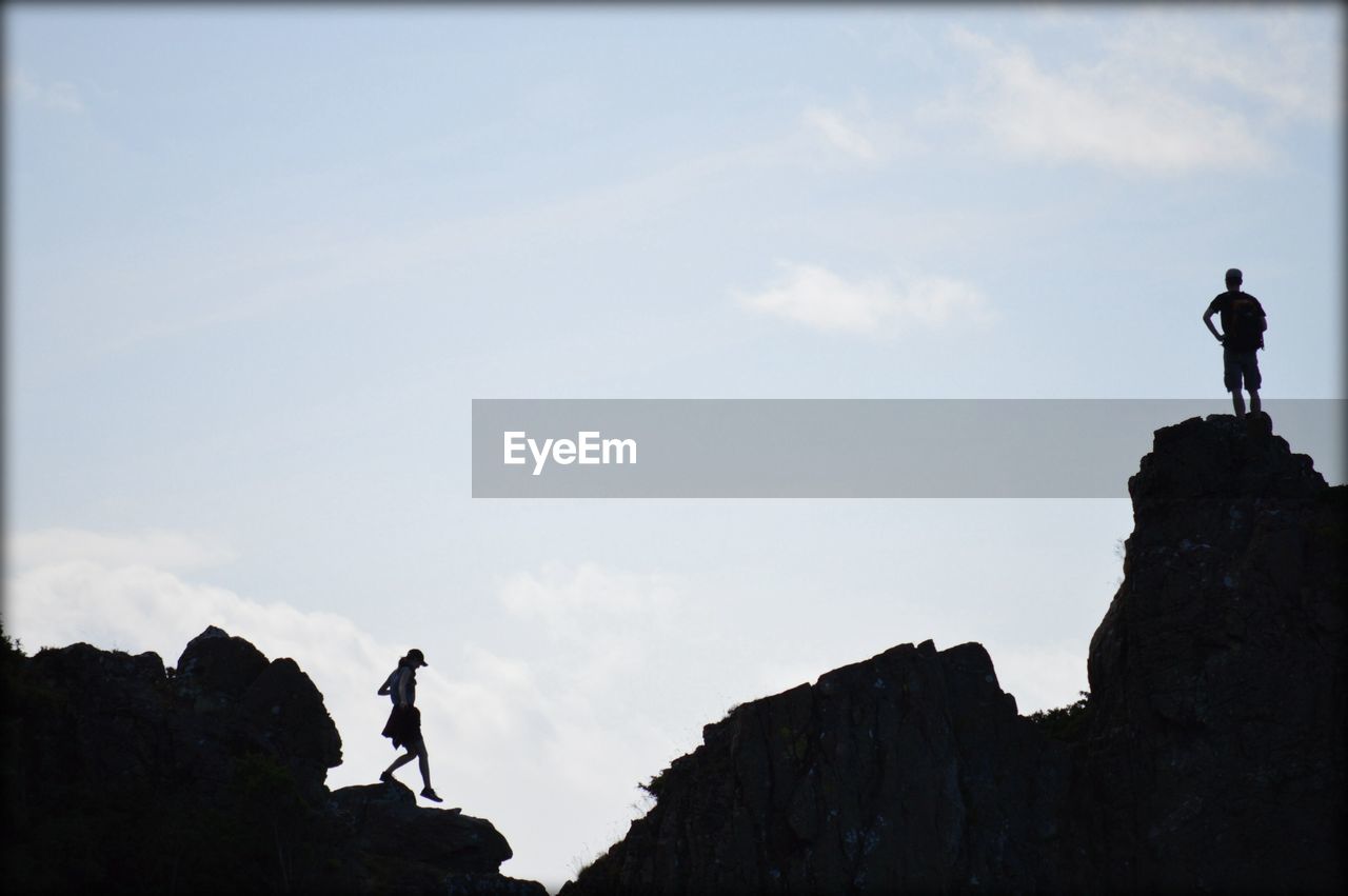 Woman walking while man standing on rock formation against sky