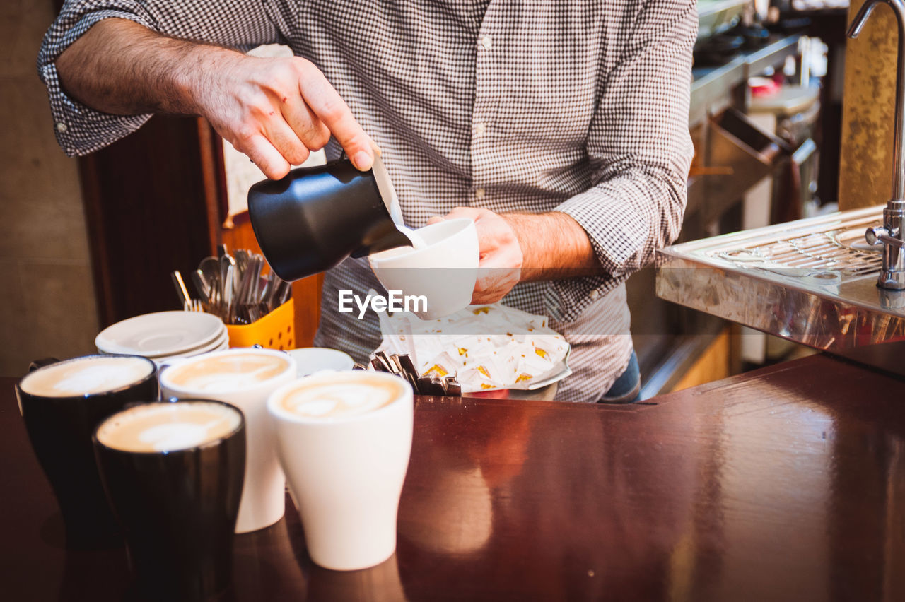 Midsection of barista pouring cream in coffee cup at cafe