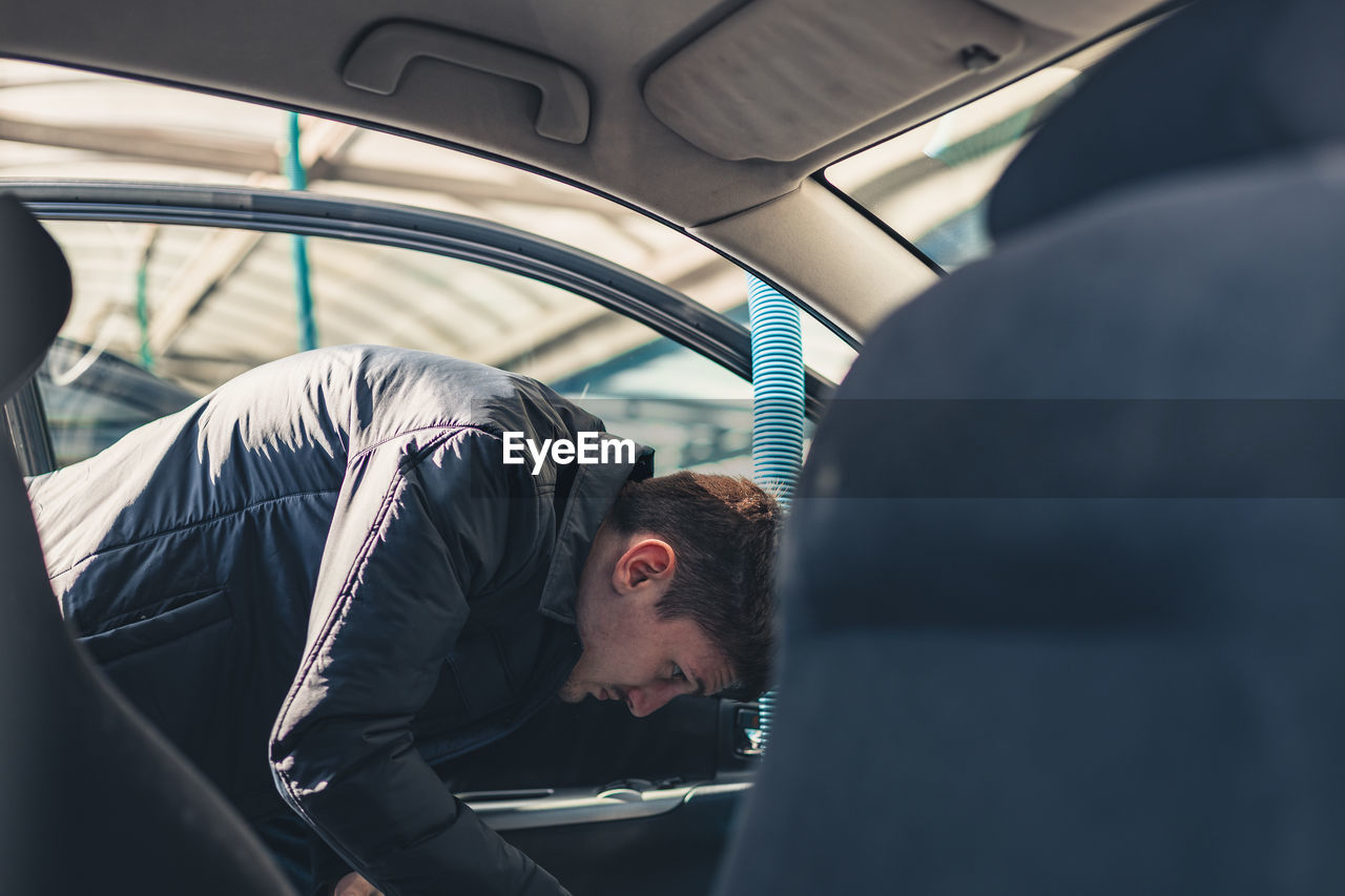 A young man vacuums the interior of a car.