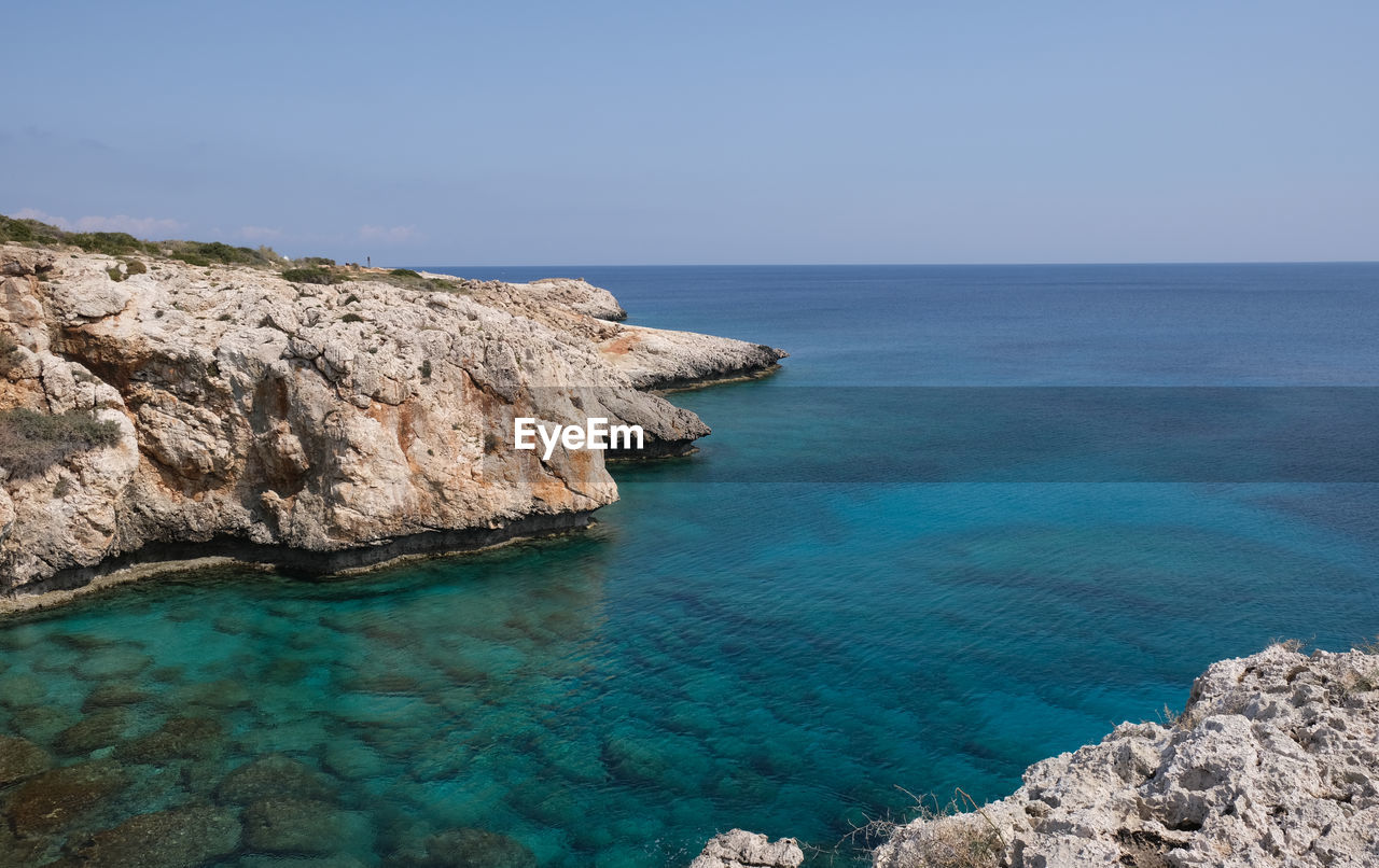 Rocky coastline with blue water and sky.