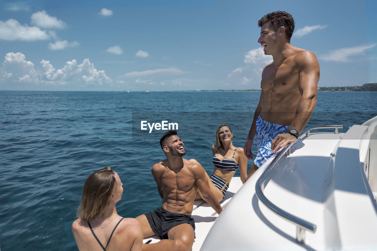 Young man and woman in swimwear enjoying summer holidays with friends on yacht floating in blue ocean in sunny day