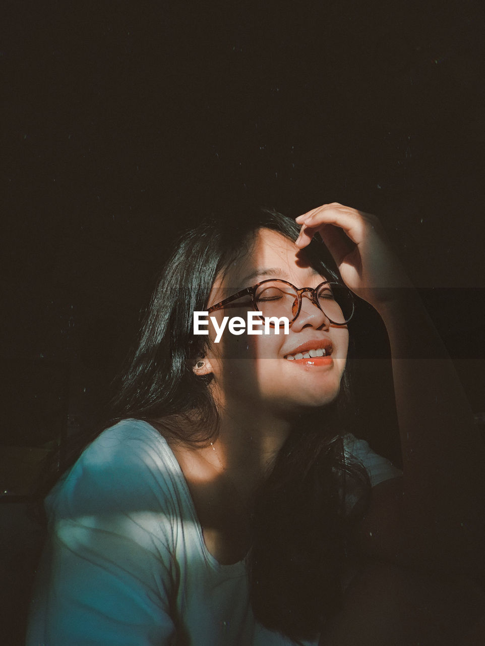 Smiling young woman eyes closed sitting in darkroom