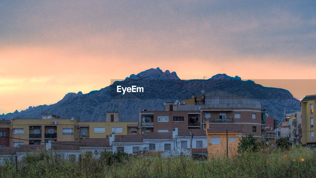 Building by mountain against dramatic sky during sunset