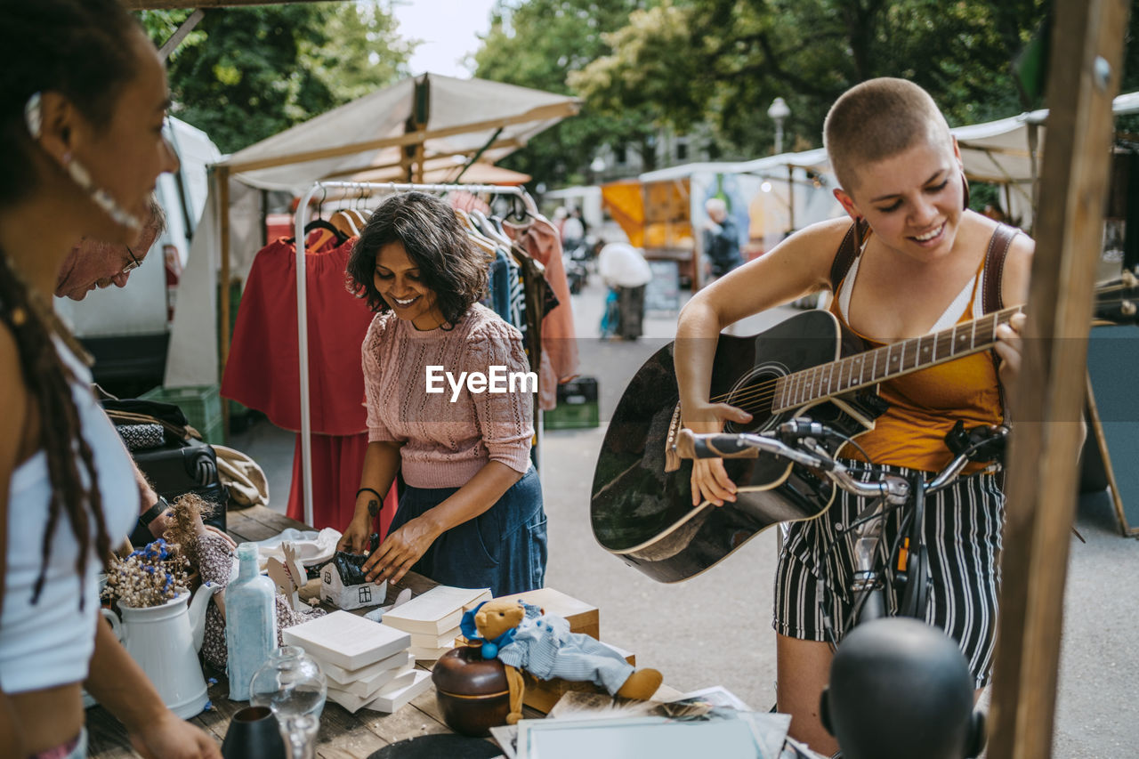 Smiling female customer playing guitar while shopping at flea market