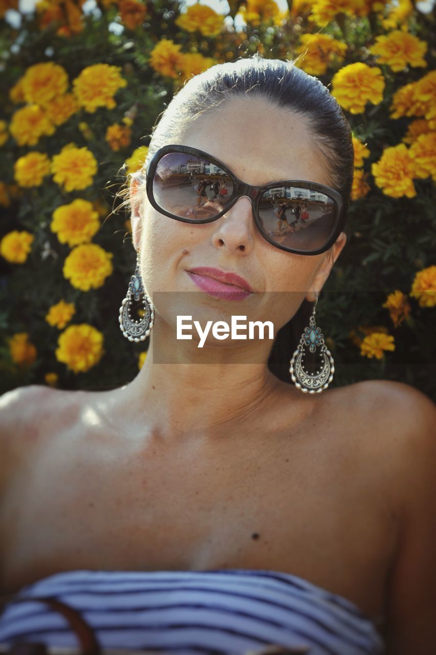 Close-up portrait of woman in sunglasses against yellow flowers