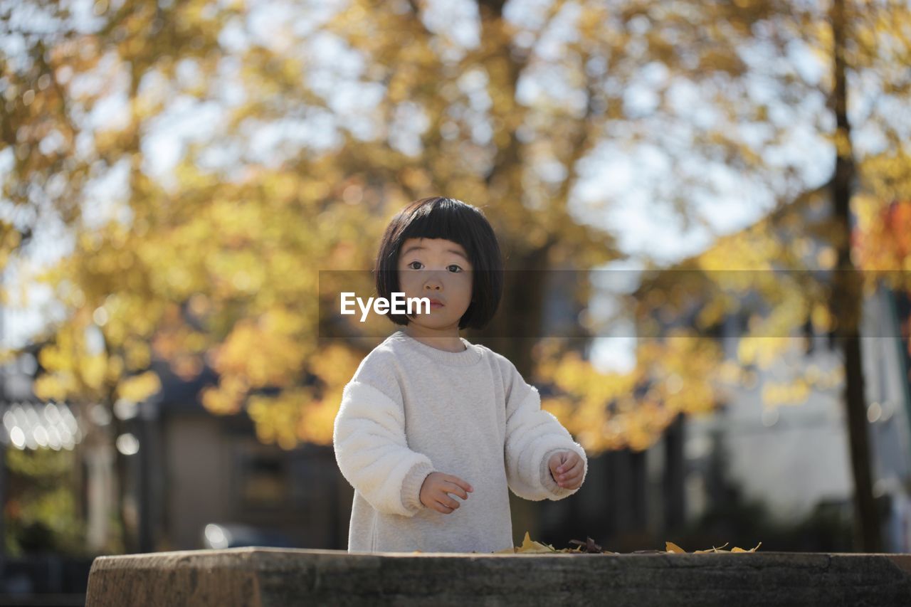 PORTRAIT OF GIRL STANDING AGAINST TREE DURING AUTUMN