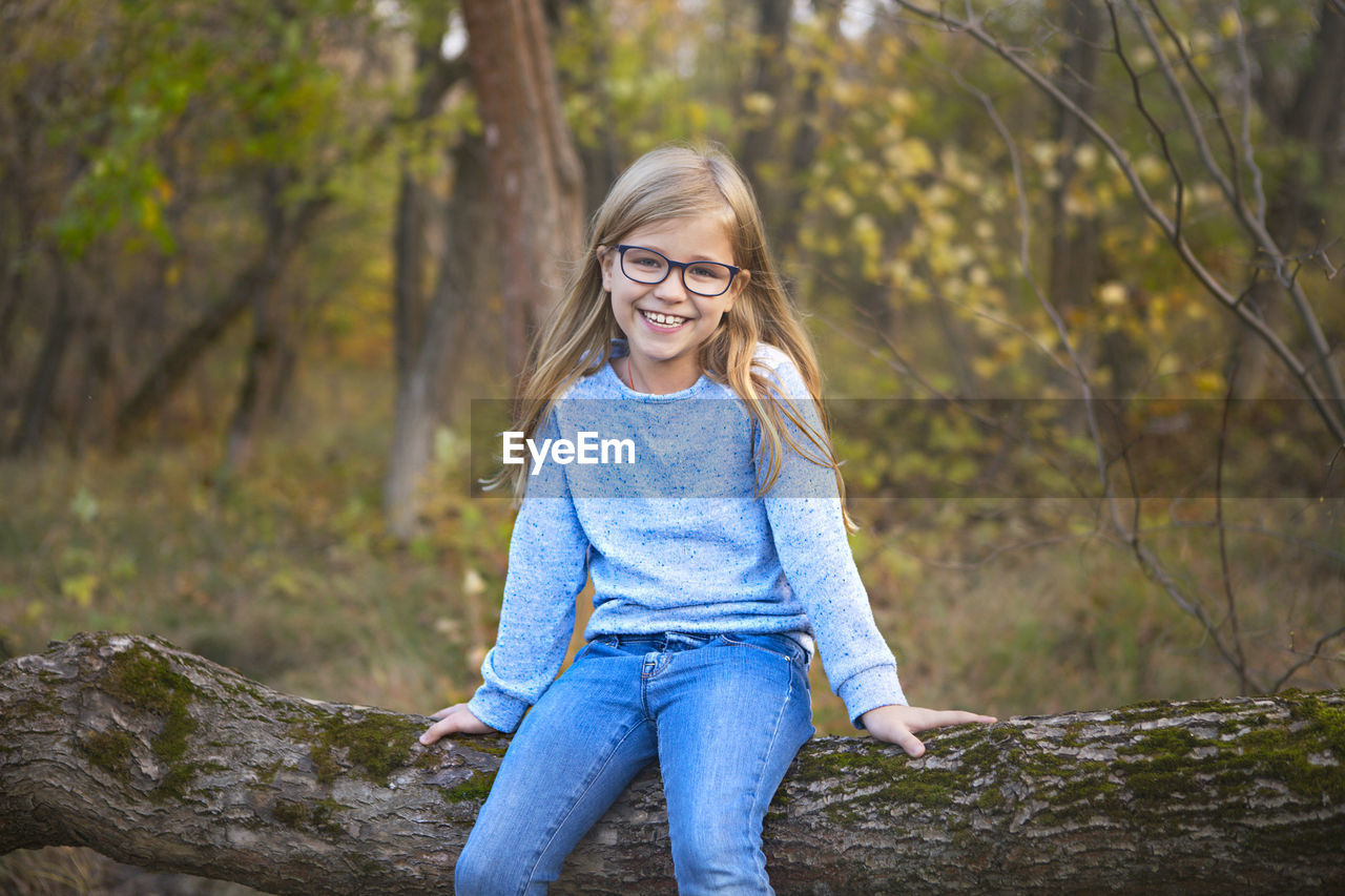 Smiling young woman standing against trees in forest