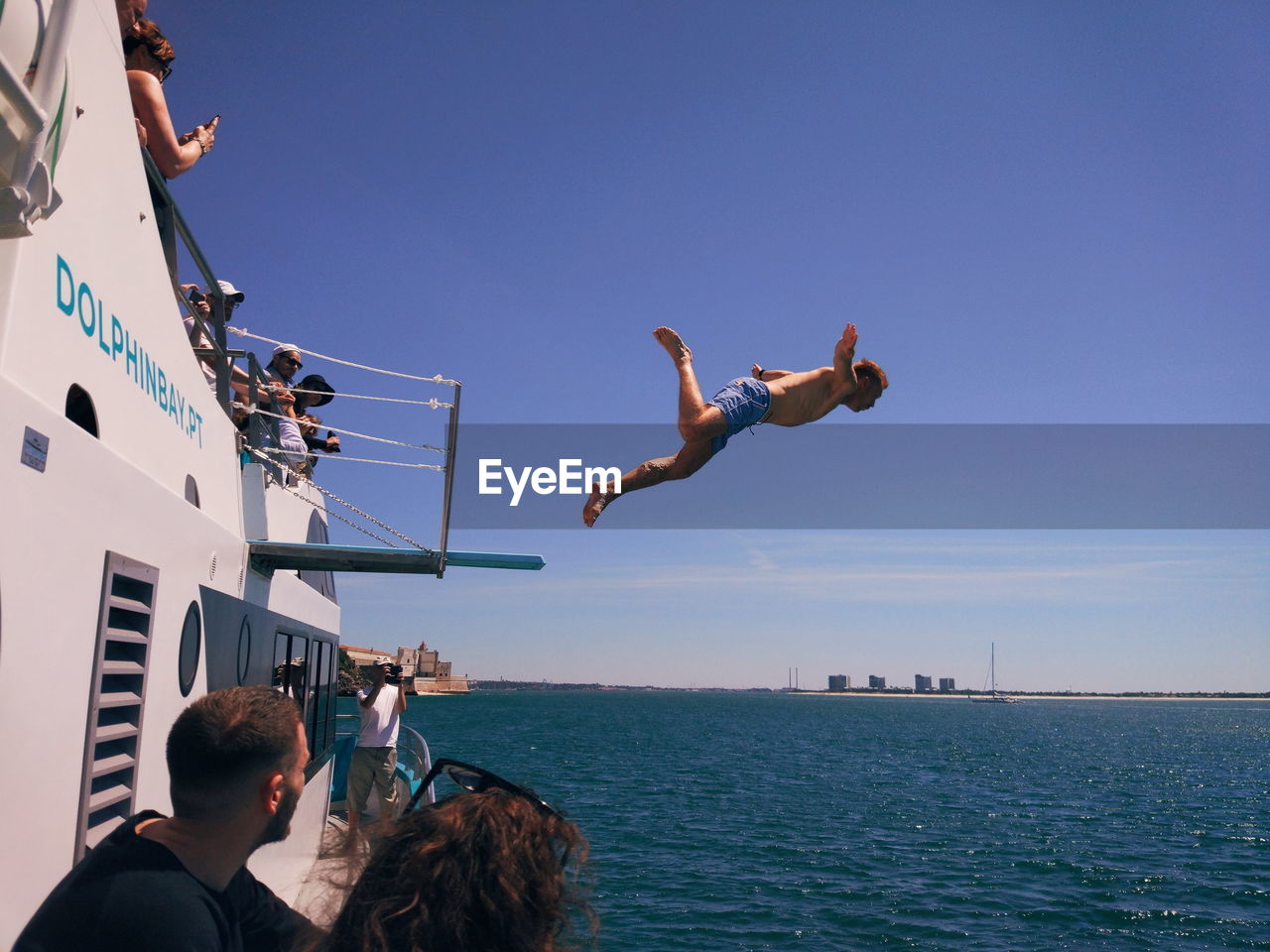 PEOPLE JUMPING OVER SEA AGAINST CLEAR SKY