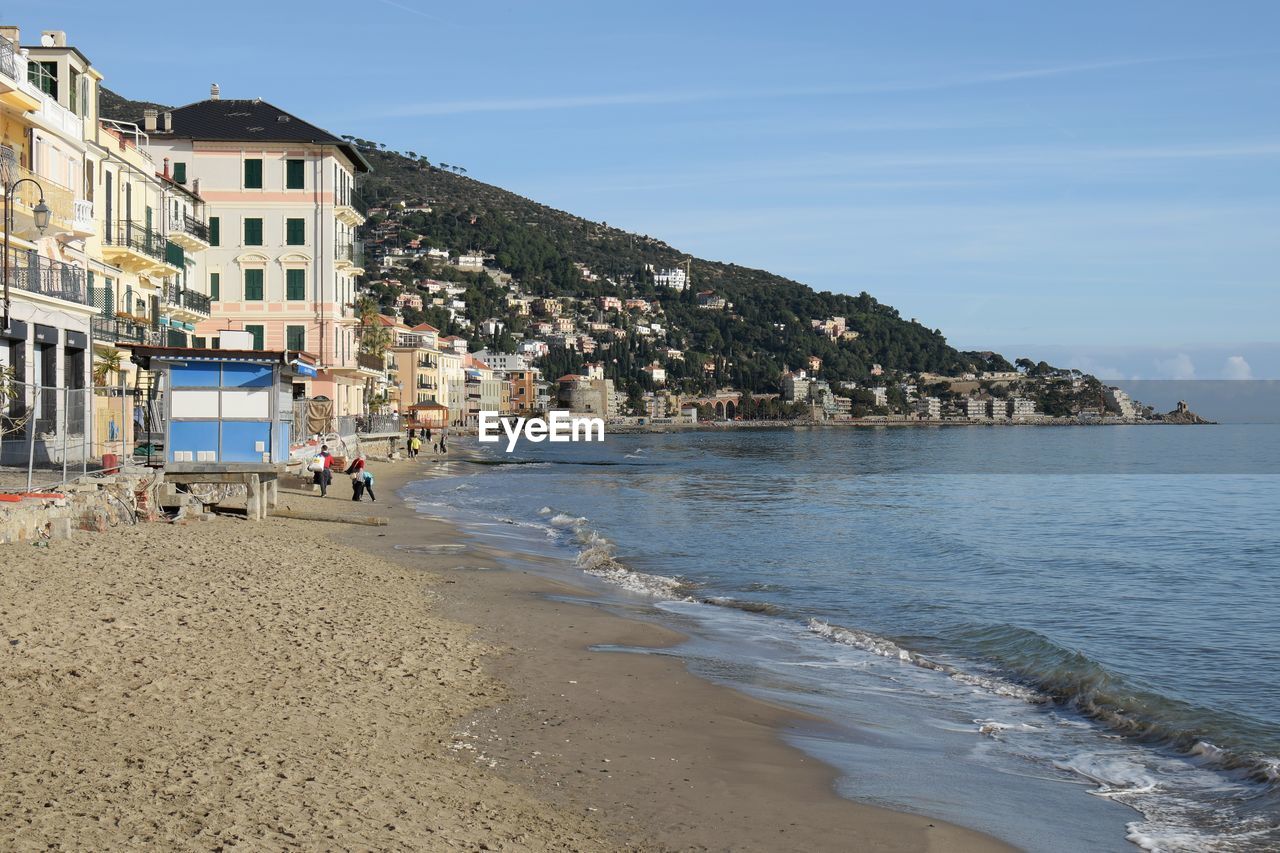 PEOPLE ON BEACH BY BUILDINGS AGAINST SKY IN CITY