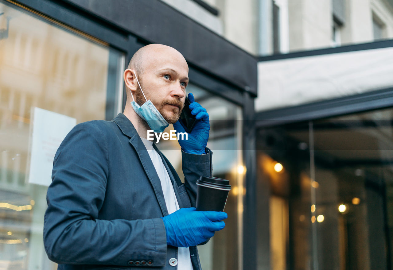 Man holding coffee up talking on phone standing outdoors