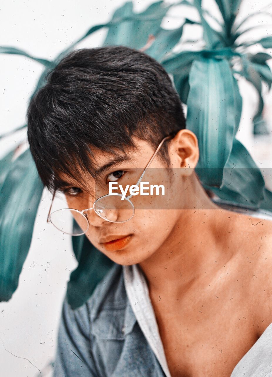 Close-up portrait of young man wearing eyeglasses against plants