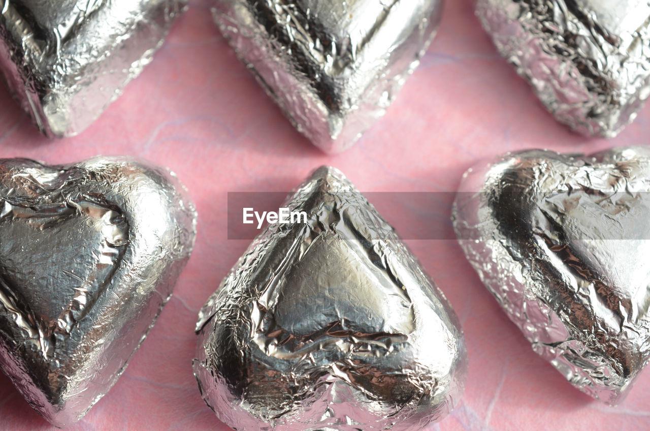 Silver foil wrapped chocolate heart shape candy on pink paper