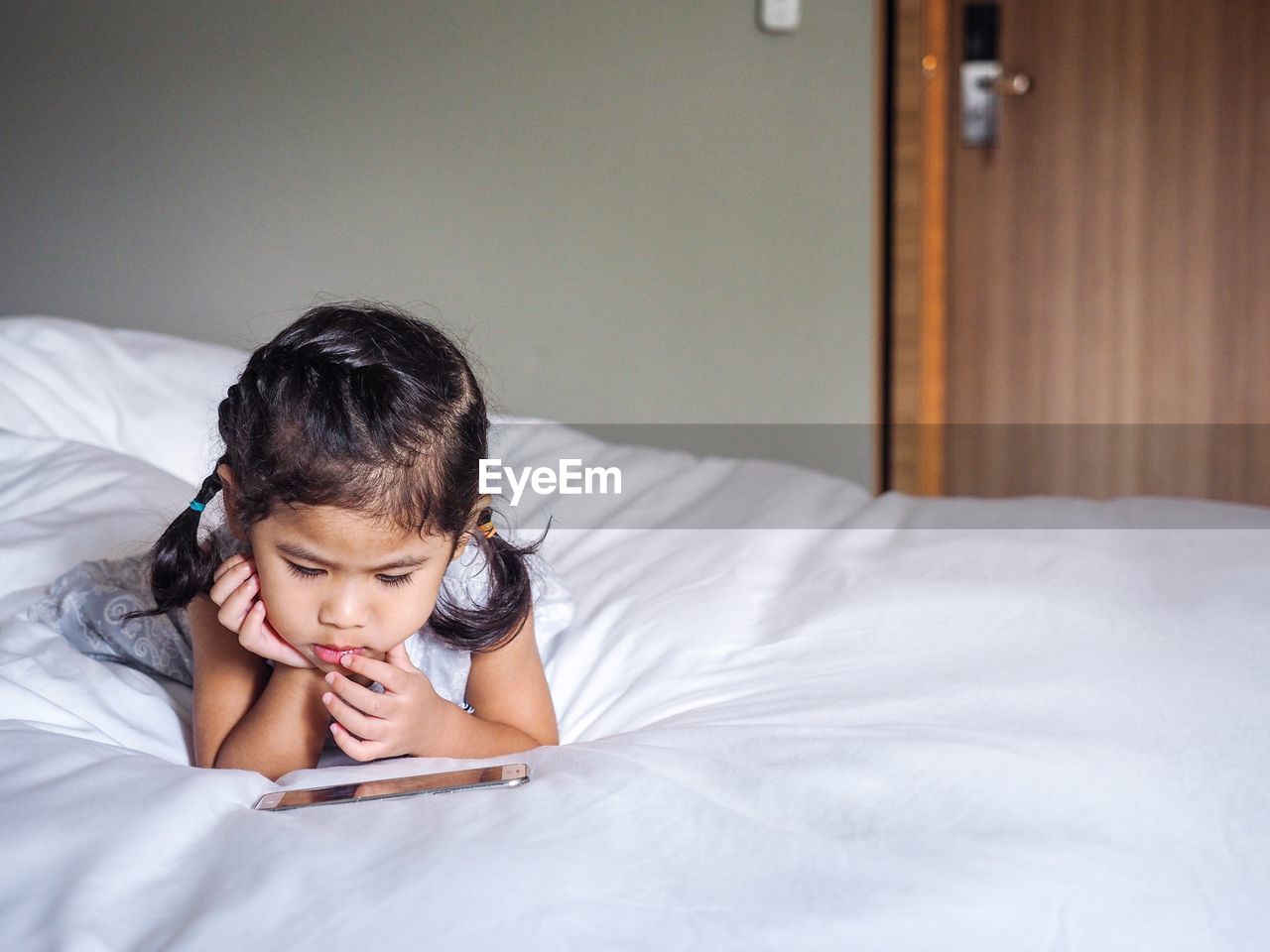 Cute girl using phone on bed at home