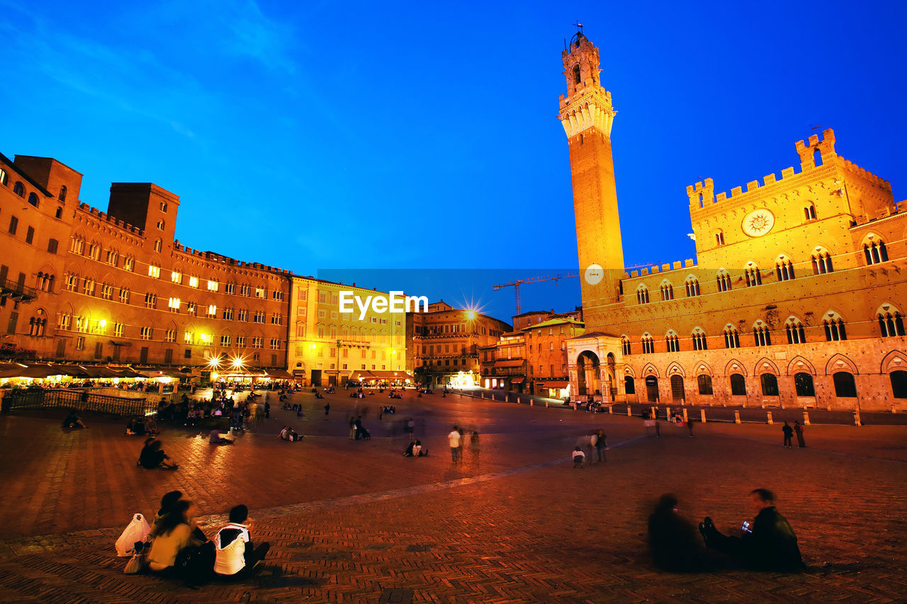 People relaxing by historic buildings at piazza del campo against sky during dusk