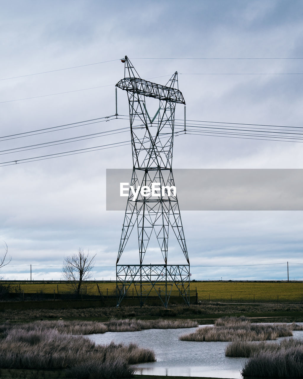 High voltage post or high voltage tower in the countryside with a small lake. cloudy background