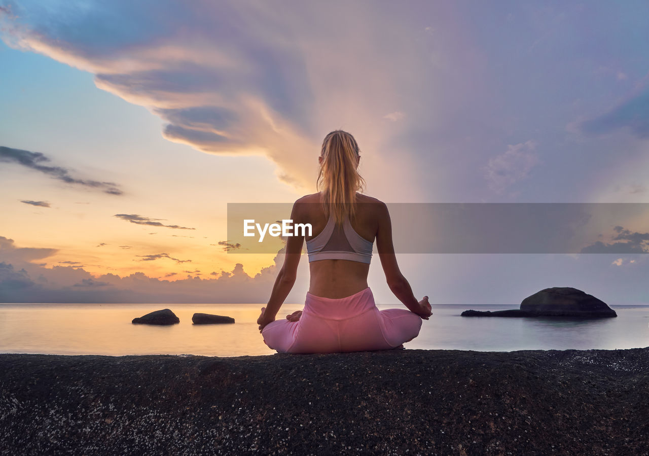 Full length of woman meditating at beach against sky