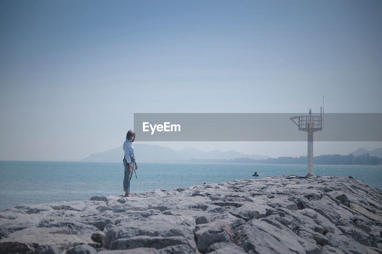 MAN STANDING ON SHORE AGAINST CLEAR SKY