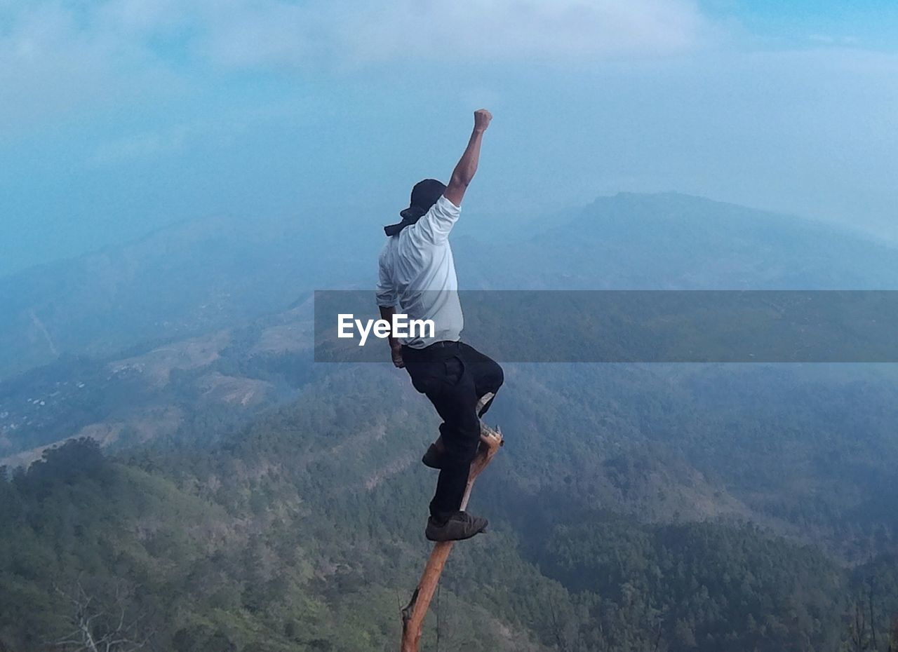 Full length of man on branch over mountain against sky