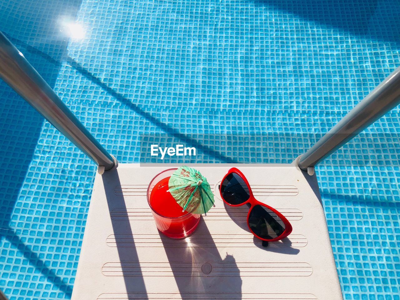 High angle view of drink and sunglasses by swimming pool
