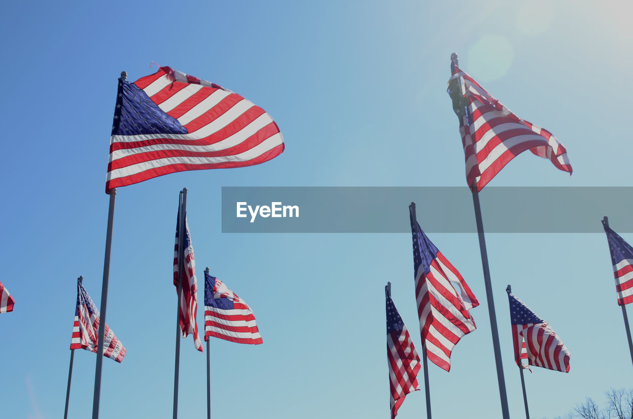 Low angle view of american flags waving against clear blue sky