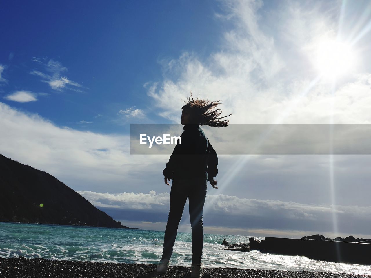 WOMAN STANDING AT BEACH AGAINST SKY