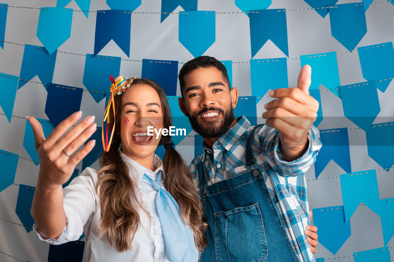 portrait of smiling friends holding shopping bags while standing against wall