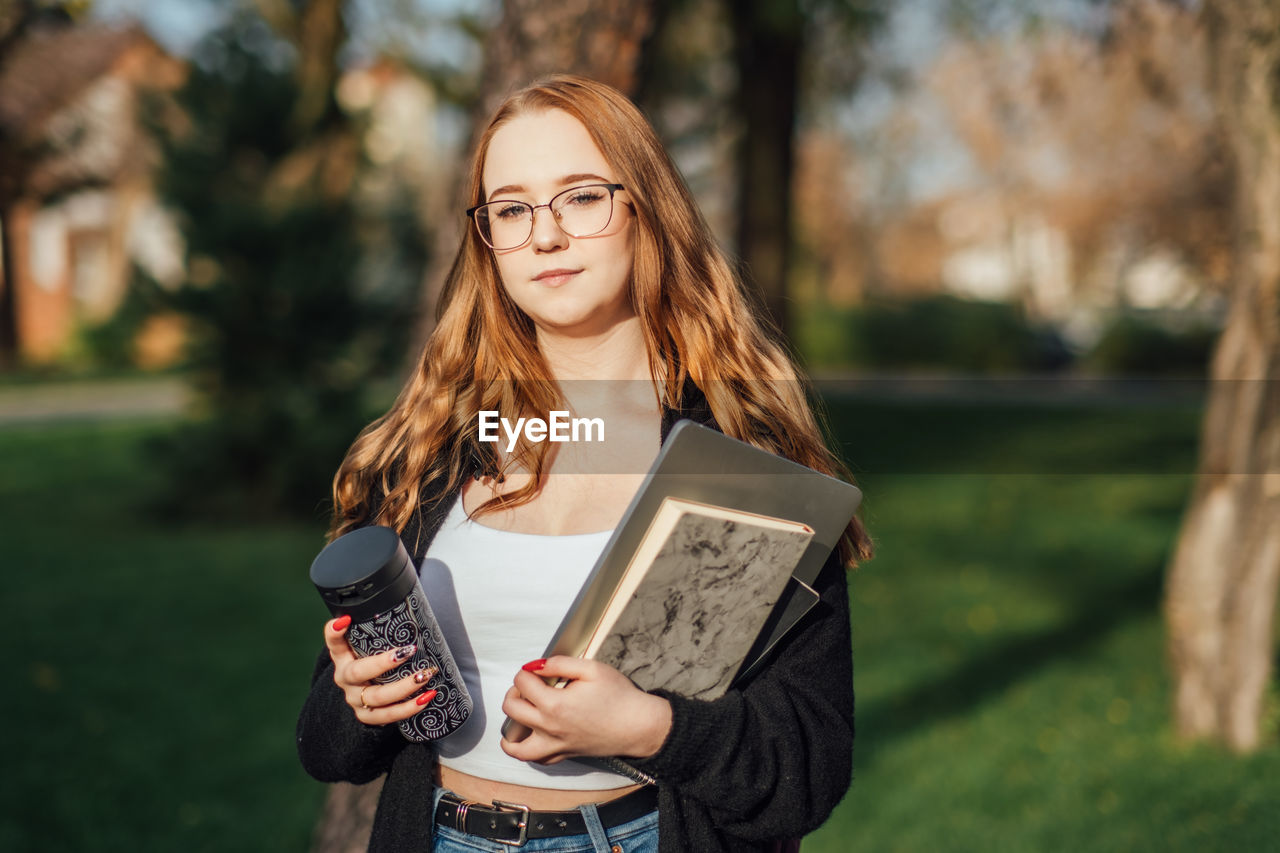 Choosing a university, college. female college student with books and laptop outdoors. redhead