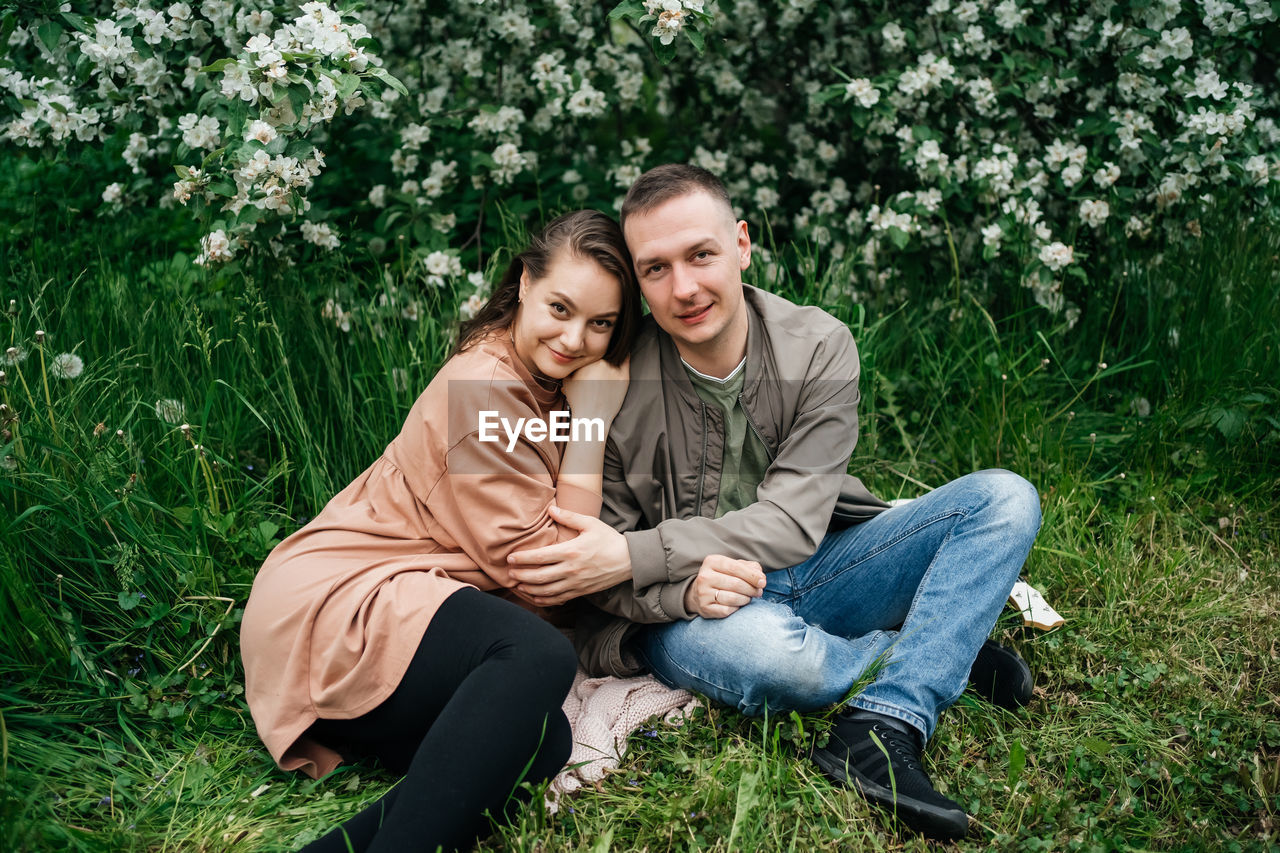 Young couple in love a girl and a man sit on the grass of a flowering apple tree 