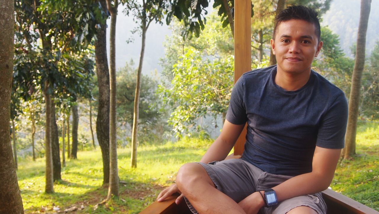 Portrait of smiling young man sitting against trees