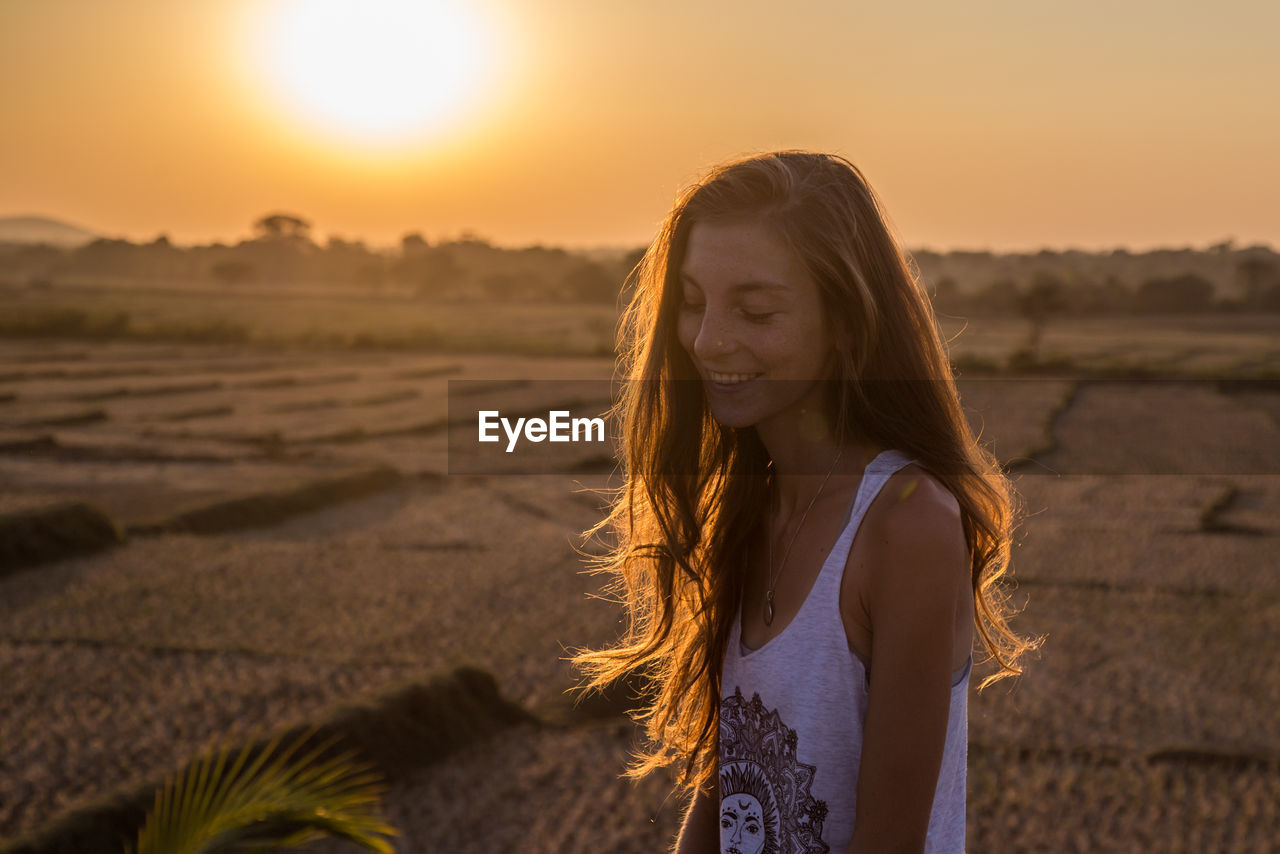 Portrait of beautiful young woman against sunset sky