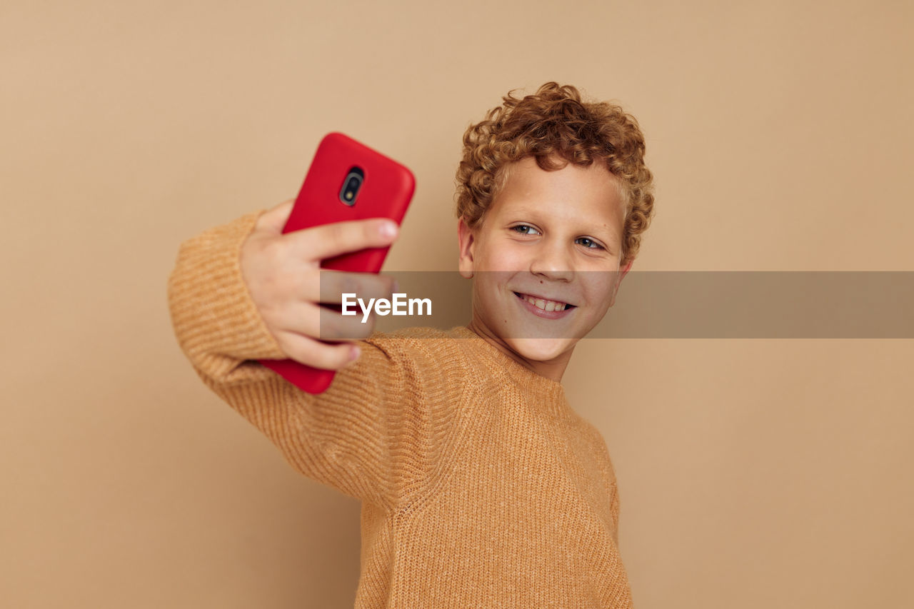 Smiling boy taking selfie with smart phone by brown background