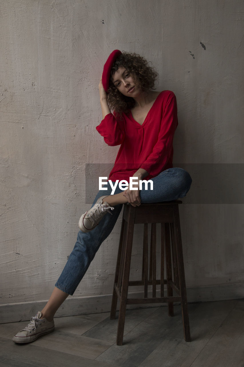 Portrait of woman sitting on chair against wall