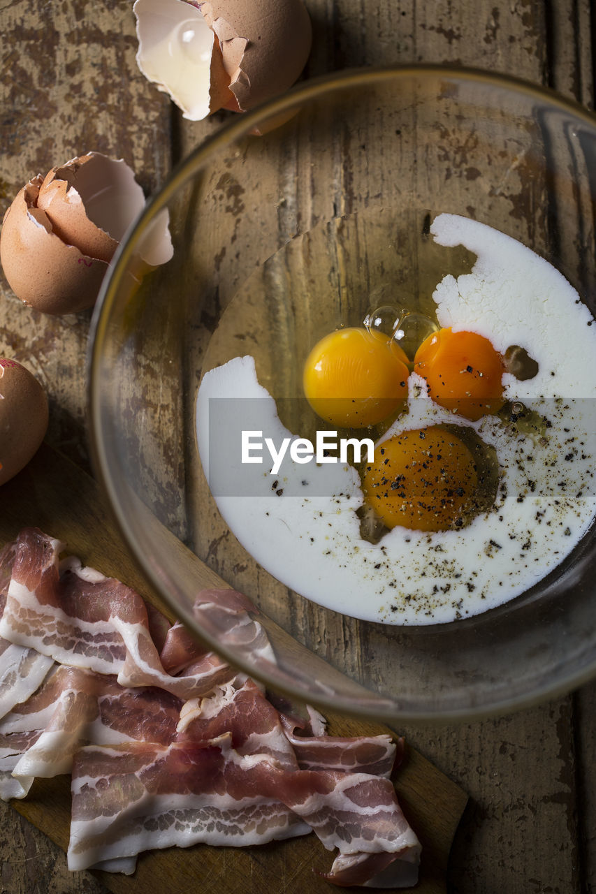 Directly above shot of egg yolk in bowl and bacon on wooden table