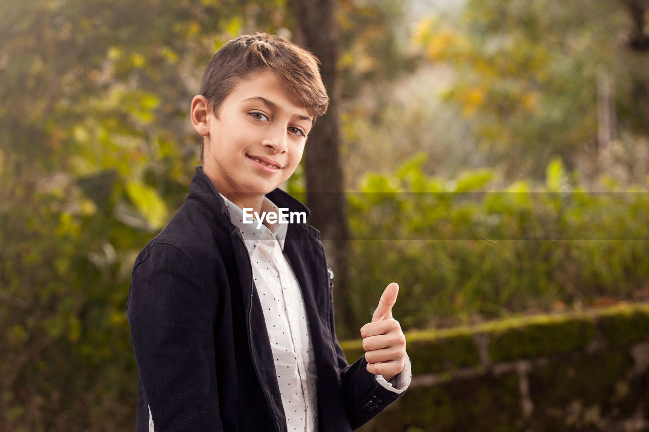 Portrait of teenage boy gesturing thumbs up in yard