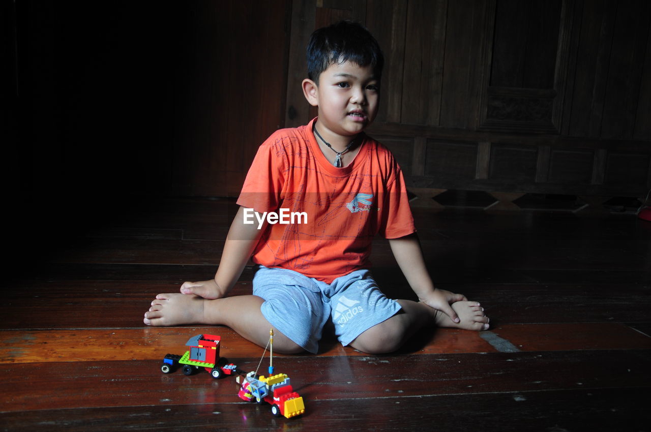 PORTRAIT OF BOY PLAYING WITH TOY SITTING ON FLOOR AT HOME