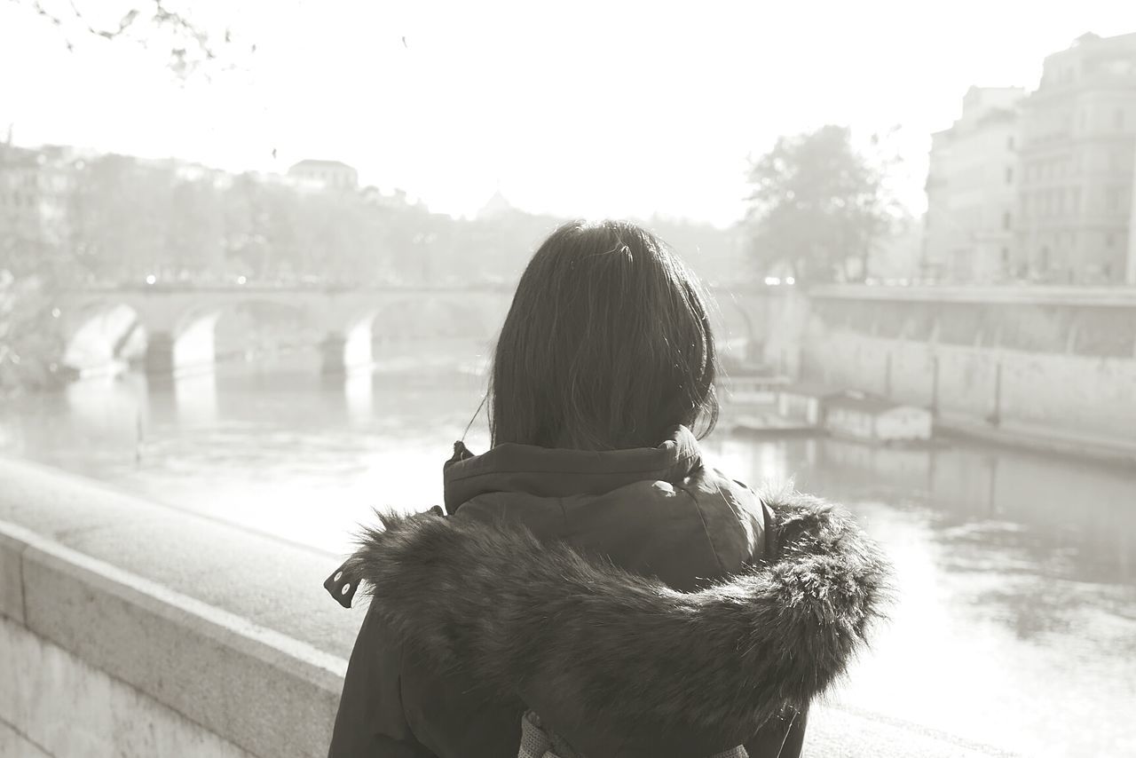 Rear view of woman by river against sky in city