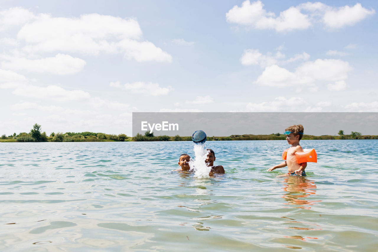 Boys playing with ball in sea against sky