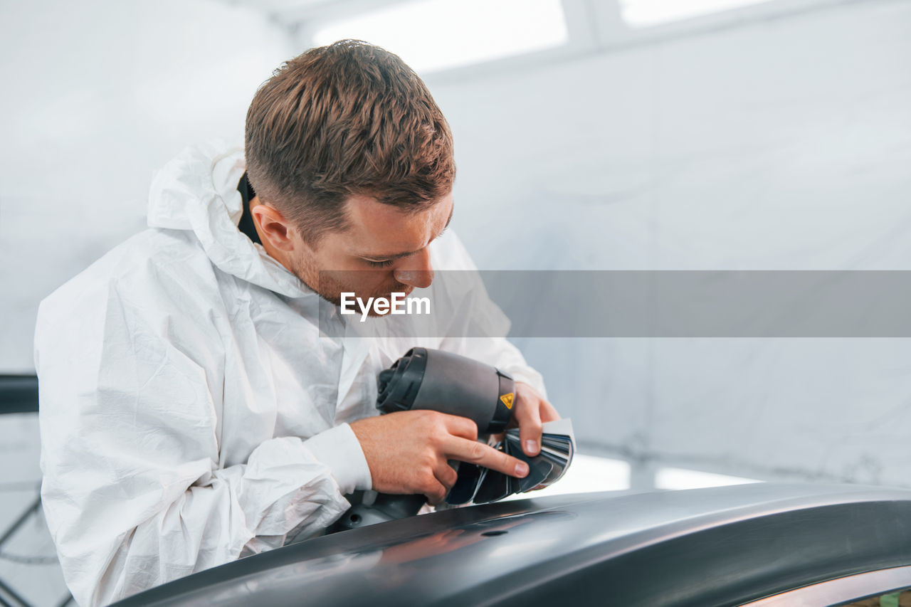 Painting the car. man in uniform is working in the auto service.