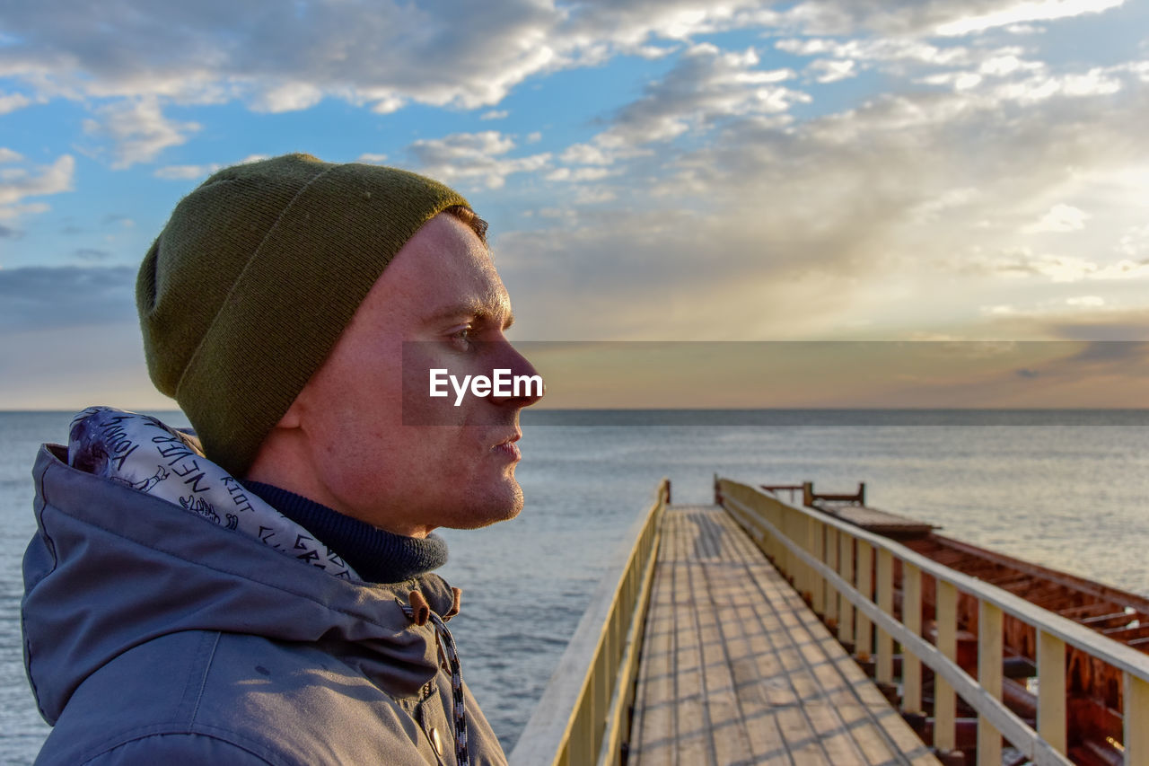 Profile view of young man standing on pier over sea against sky