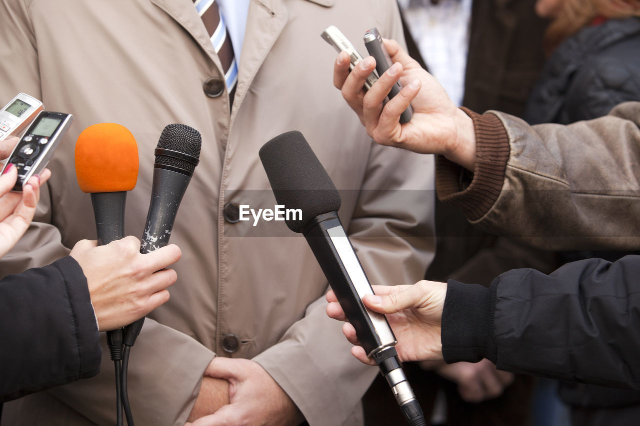Midsection of politician giving interview while journalists holding microphones